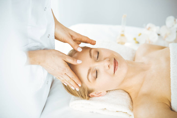 Beautiful happy woman enjoying facial massage with closed eyes in spa salon. Relaxing treatment in medicine and Beauty concept - Foto, Bild