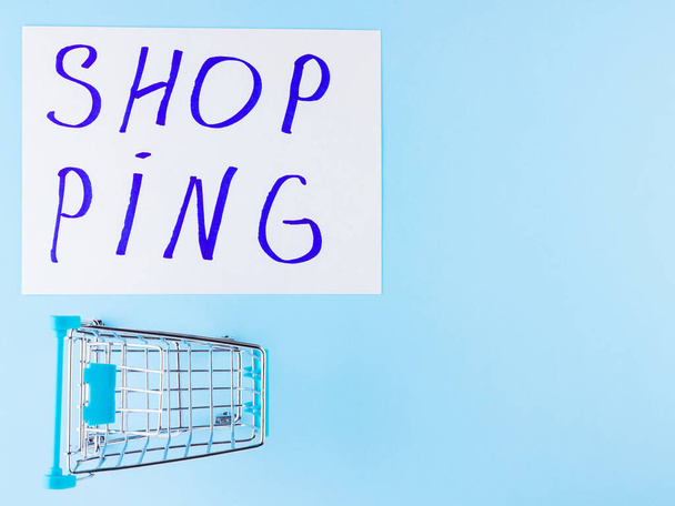Shopping cart on blue background. Shop trolley at supermarket. Sale and discount. Consumer society trend. Concept of shopping. Copy space. Top view - 写真・画像