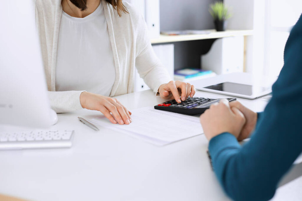 Accountant checking financial statement or counting by calculator income for tax form, hands closeup. Business woman sitting and working with colleague at the desk in office toned in blue. Tax and - Photo, Image