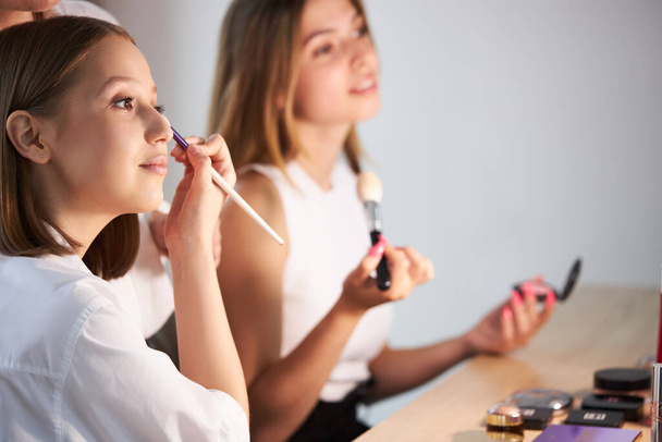 attractive girls applying cosmetics on face, doing make-up on themselves - Fotoğraf, Görsel