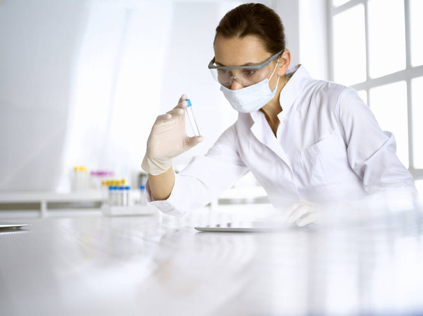Female laboratory assistant analyzing a blood sample at hospital. Medicine, health care and researching concept - Foto, Bild