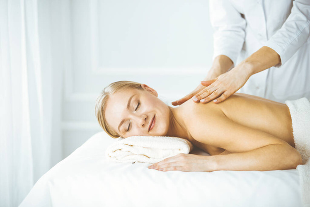 Schöne glückliche Frau genießt Rückenmassage mit geschlossenen Augen. Schönheits- und Wellness-Salonkonzept - Foto, Bild