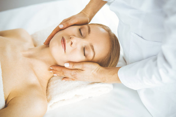 Beautiful happy woman enjoying facial massage with closed eyes in spa salon. Relaxing treatment in medicine and Beauty concept - Foto, Bild