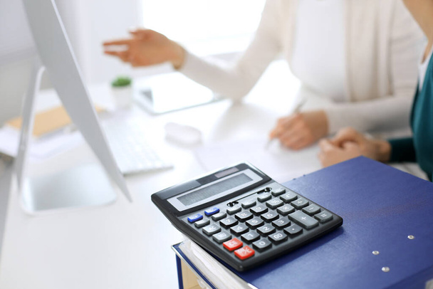 Калькулятор и папки с бумагами ждут, чтобы их обработала деловая женщина или бухгалтер, работающий за столом в офисе. Концепция внутреннего аудита и налогообложения - Фото, изображение