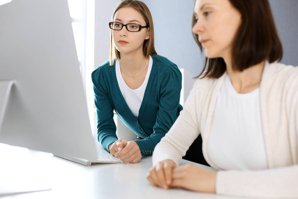 Businesswoman giving presentation to her female colleague while they sitting at the desk with computer. Group of business people working in office. Teamwork concept - Photo, image