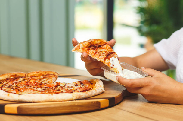 A girl dips a slice of pizza in sauce in a plastic container before eating it - 写真・画像