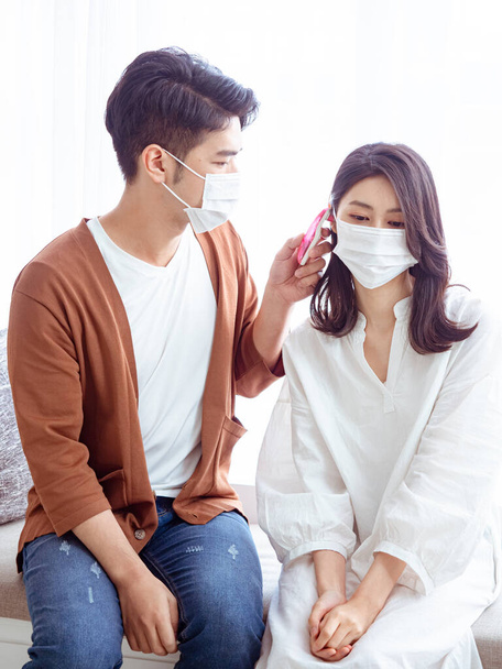 Fiatal ázsiai pár sebészeti maszkot visel és fülhőmérőt használ - Fotó, kép
