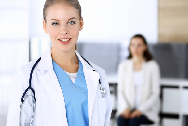Doctor woman filling up medication history record while standing in emergency hospital office with patient in queue at background. Physician at work, portrait shoot. Medicine and health care concept - Photo, image