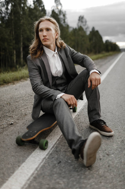 Handsome man in office suit with longboard walking down road in city outskirts. - Fotografie, Obrázek