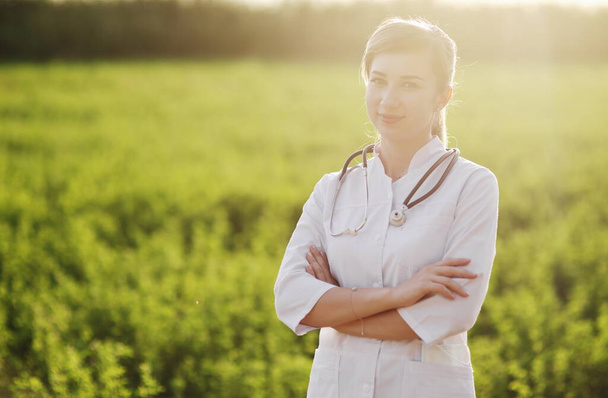 Portrét krásné ženské lékaře nebo zdravotní sestry na zeleném travnatém pozadí. Prevence Covid-19 koncepce zdravotní péče. Stetoskop přes krk. Žena, dívka. - Fotografie, Obrázek