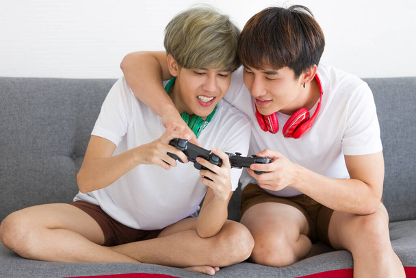Щасливі азіатські гомосексуалісти або пари геїв разом грають у відеоігри на дивані. Концепція гордості ЛГБТ. - Фото, зображення