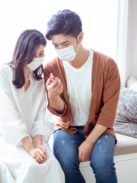 Fiatal ázsiai pár sebészeti maszkot visel és fülhőmérőt használ - Fotó, kép