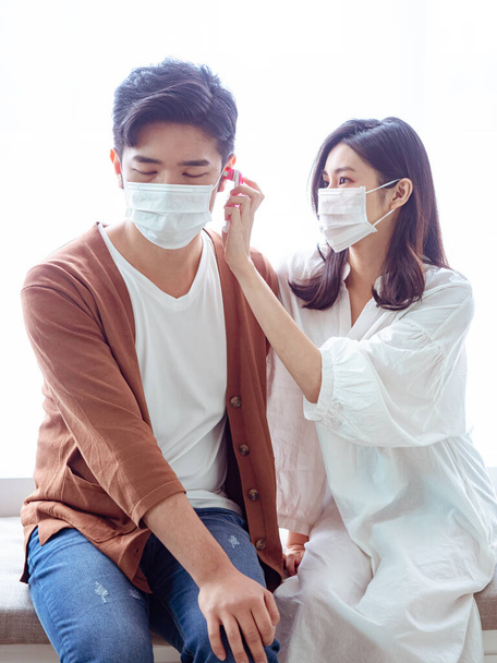 Joven pareja asiática con máscara quirúrgica y el uso de termómetro de oído - Foto, imagen