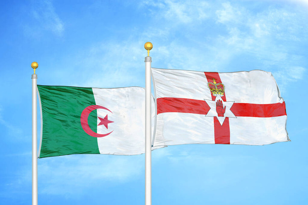 Αλγερία και Βόρεια Ιρλανδία δύο σημαίες σε κοντάρια σημαίας και φόντο μπλε συννεφιασμένο ουρανό - Φωτογραφία, εικόνα