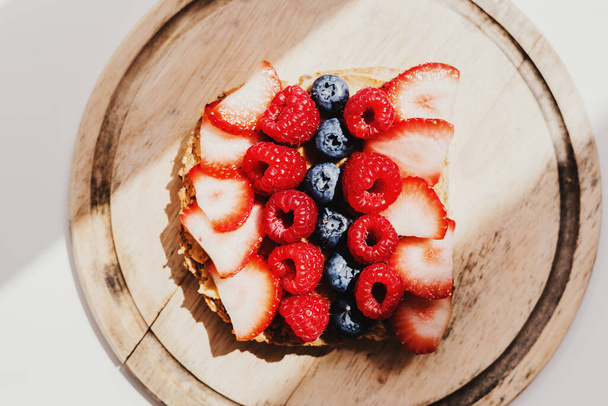 Peanut butter toast with fresh seasonal berries: raspberry, blueberry and strawberry on wooden board under bright sun light. Morning breakfast food - Photo, Image