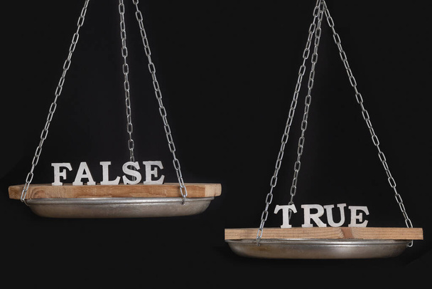 Worte Wahrheit und Lüge auf der Waage. Ungleichgewicht. Schwarzer Hintergrund in Nahaufnahme. - Foto, Bild