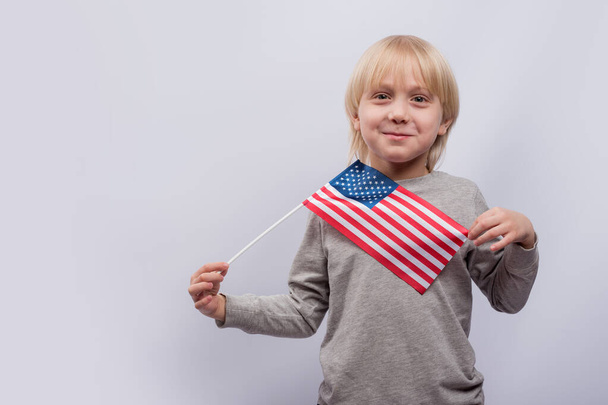 Passionnant garçon aux cheveux blonds tenant un drapeau américain sur fond blanc. L'éducation en Amérique. - Photo, image