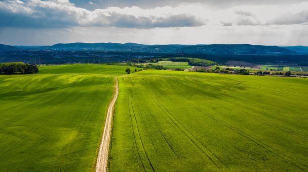 Estrechar el camino de grava entre los campos verdes en el paisaje rural a la ciudad en la distancia en Austria - Foto, Imagen