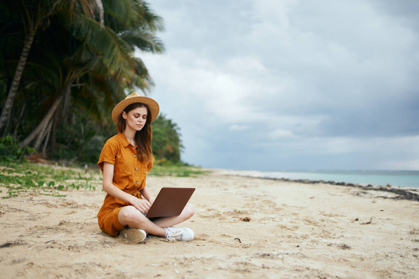 彼女の膝の上にラップトップを持つ旅行者は、ビーチ島の熱帯の砂の上に座っている  - 写真・画像
