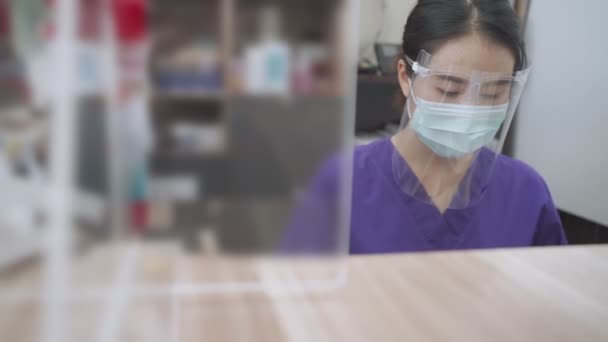 OPD reyonunda koruyucu ekipman takan Asyalı kadın hemşire koruyucu gözlükler, maske ve yüz kalkanı pandemik kovid-19 Corona virüsü, tıbbi klinikte, bulaşıcı hastalıkların önlenmesi - Video, Çekim