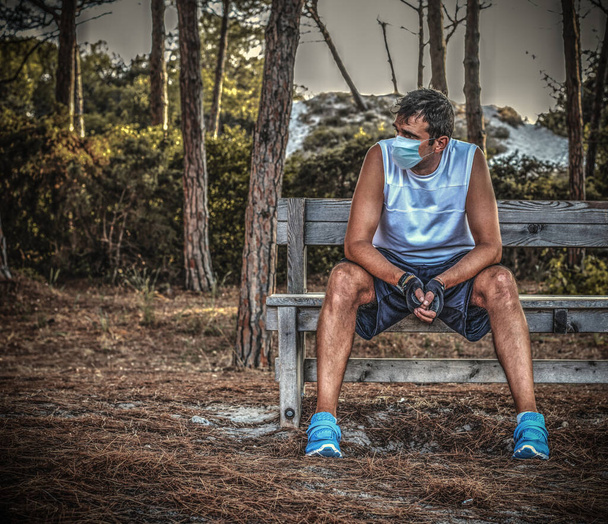 atleta con maschera antivirale appoggiata su una panchina di legno in un parco - Foto, immagini