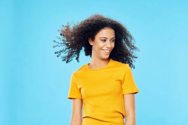 Femme gaie avec cheveux bouclés afro coiffure en t-shirt jaune look attrayant sourire  - Photo, image