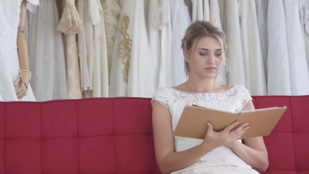 Braut liest Buch oder Katalog im Hochzeitsstudio. - Filmmaterial, Video