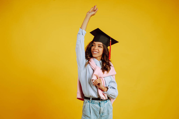 Portrait of African American girl in a graduation hat on her head posing on a yellow background. Graduation, university, college, distance education concept. - Foto, immagini