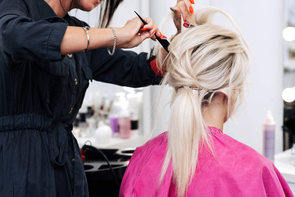 Die Hände eines Friseurs mit Kamm machen eine Frisur für ein blondes Mädchen - Foto, Bild