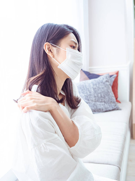 Young asian woman wearing surgical mask and suffering from pain in shoulder - Fotografie, Obrázek