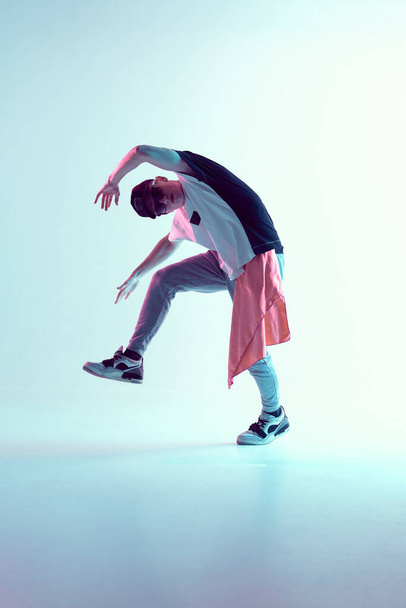 Guy dancing contemporary dance in studio. Neon light blue background. Acrobatic bboy dancer. Break dance lessons. - Photo, image
