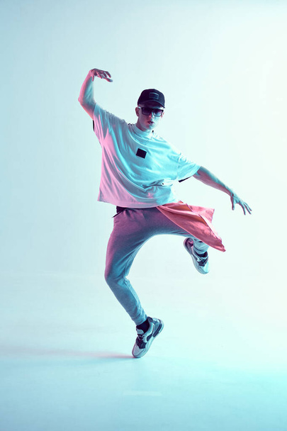 Guy dancing contemporary dance in studio. Neon light blue background. Acrobatic bboy dancer. Break dance lessons. - Фото, изображение