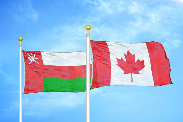 Oman et le Canada deux drapeaux sur des mâts et fond bleu ciel nuageux - Photo, image
