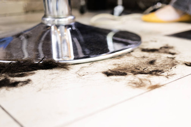 Corte o cabelo castanho deitado no chão perto da cadeira de barbeiro de metal. Saloon precisa de serviço de limpeza
 - Foto, Imagem