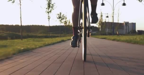 Woman twists pedals on road bike on cycle path at sunset. Female cyclist is spinning pedals on aero bicycle. Athlete is speeding on bicycle in sunset light. Cycling gear and chain. Bike wheel rotation - Materiał filmowy, wideo