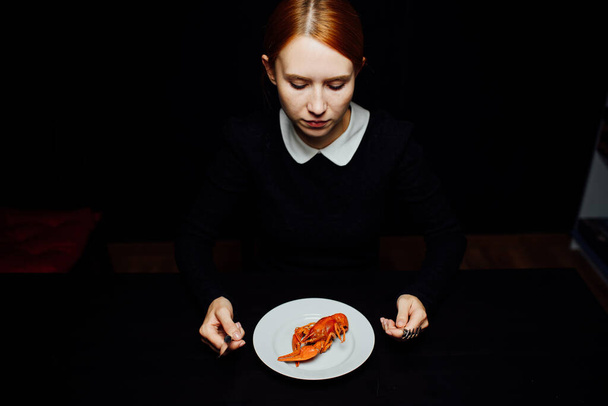 boiled crayfish on a white plate, knife and fork in hand on a black background minimalism - Fotoğraf, Görsel