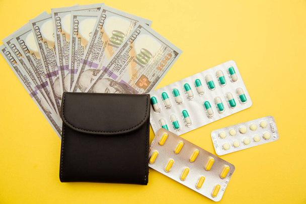 Grey wallet with money and tablets of pills on yellow background. - Foto, Imagen