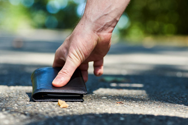 Foto de una acera y la mano de un hombre que encontró una cartera de cuero negro mientras caminaba - Foto, imagen