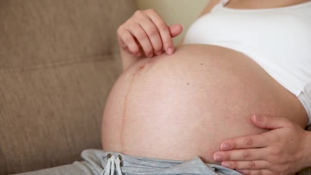 Een zorgzame moeder streelt een naakte zwangere buik met twee handen, op lichte kamer. Een zwangere vrouw streelt een grote buik in de zonnige zomerdag - Video