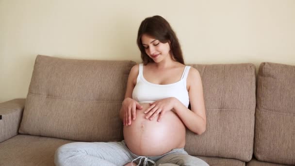 Portrait de mère attentionnée caresse un ventre nu enceinte avec deux mains, sur la pièce lumineuse. Une femme enceinte caresse un gros ventre dans la journée ensoleillée d'été - Séquence, vidéo