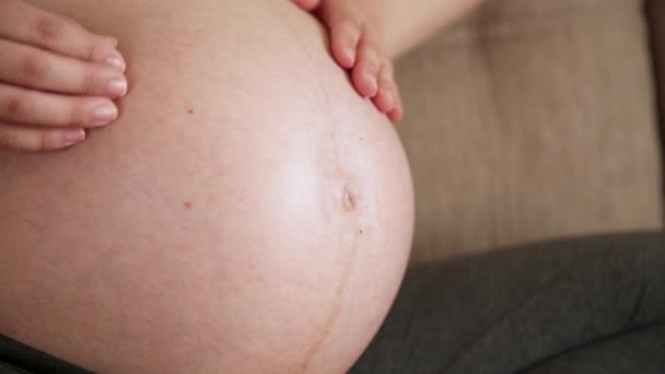 Egy gondoskodó anya megsimogat egy meztelen terhes hasat két kézzel, a fényszobában. Egy terhes nő megsimogat egy nagy hasat a napsütéses nyári napon.. - Felvétel, videó