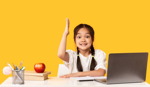 Asiática estudante no laptop levantando mão sobre fundo amarelo estúdio
 - Foto, Imagem