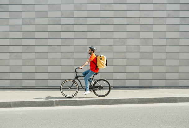 Delivery man on bicycle. Young guy with beard and big backpack rides along path in city - Foto, imagen