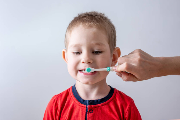 Bebek, bir ebeveynin yardımıyla dişlerini fırçalar. Çocuk diş bakımı ve hijyen eğitimi kavramı. - Fotoğraf, Görsel