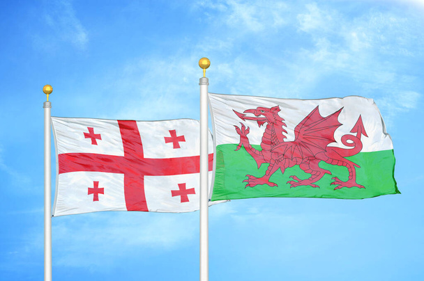 Grúzia és Wales két zászló zászlórúd és kék felhős ég háttér - Fotó, kép