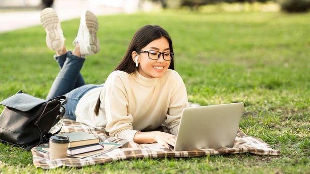Asian woman using laptop, lying in the park - Photo, Image