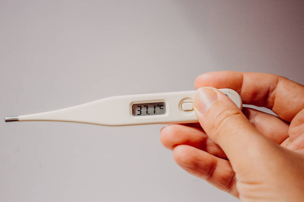 Krankheit und Fieber. Erste Symptome des Coronavirus. Elektronisches Thermometer mit einem Anzeigewert von 37,1 Grad in der Hand einer Frau auf hellweißem Hintergrund Nahaufnahme mit Platz für Text. - Foto, Bild