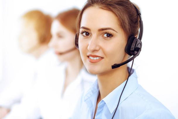 Call center operators. Focus on beautiful business woman using headset in sunny office - Foto, imagen