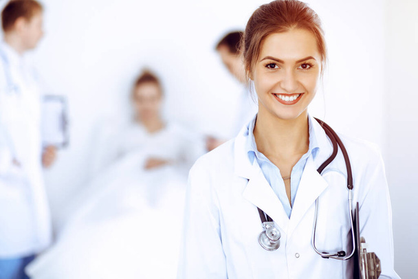 Female doctor smiling on the background with patient in the bed and two doctors - Foto, afbeelding