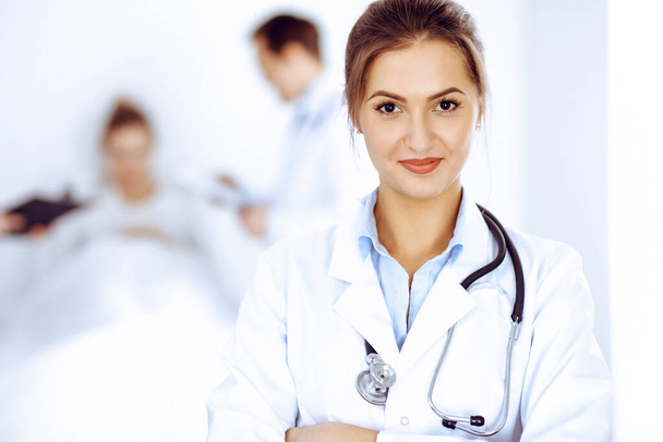Female doctor smiling on the background with patient in the bed and two doctors - Foto, Bild
